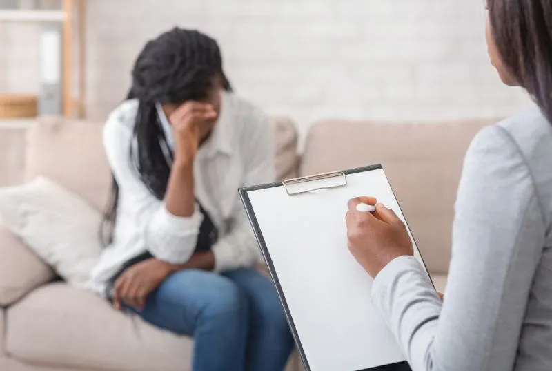 Client in an emotional session highlighting psychotherapy vs therapy differences with a professional taking notes.