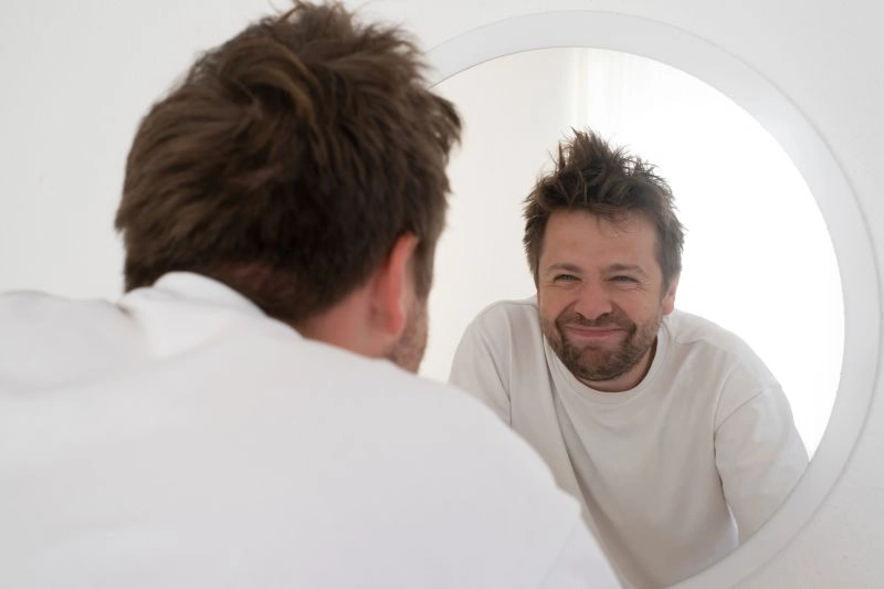 A man smiling in front of a mirror, symbolizing the journey toward positive self-reflection, a key part of treatment for borderline personality disorder.