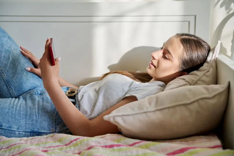 Teenager relaxing and using her phone, exploring online mental health services like American telepsychiatry for accessible care.