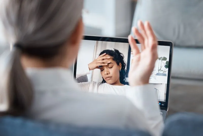 Telepsychiatry services being used by a woman experiencing stress during a video call with a mental health professional, exploring the benefits of virtual care.