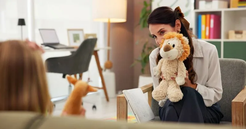 A therapist using a stuffed lion to engage a child in family counseling, providing a safe space for emotional growth and support through family psychiatry services.