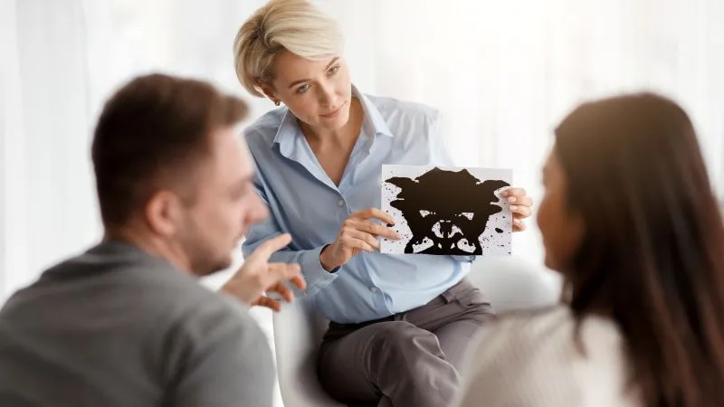 A therapist showing an inkblot image to a couple during a psychotherapy session, exploring the differences between psychotherapy vs cognitive behavioral therapy.