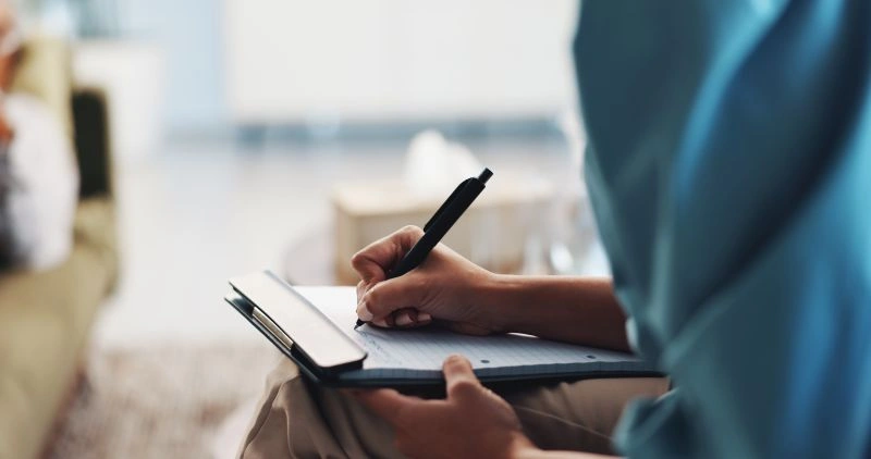 A mental health professional writing notes during a session at a mental health urgent care clinic, focusing on immediate care for patients seeking urgent support.