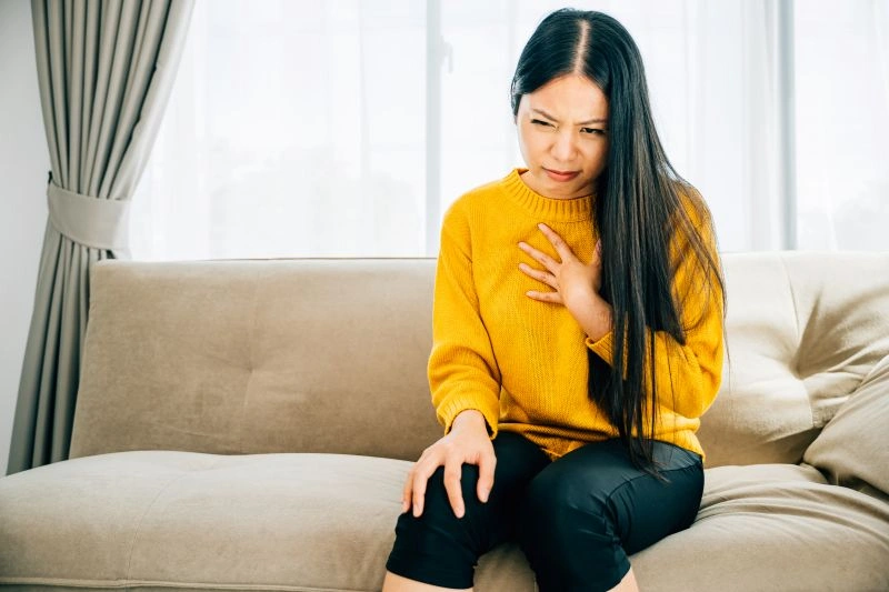 "A woman experiencing chest pain, seeking urgent care for mental health in a clinic setting, addressing emotional distress in a timely and supportive environment.