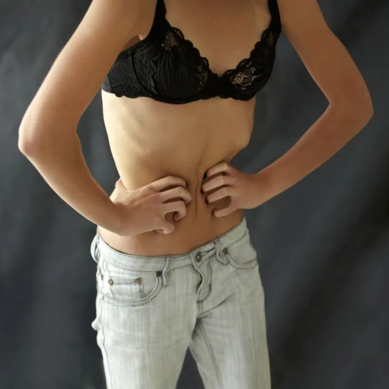 A young woman standing and holding her waist, showing signs of physical discomfort or dissatisfaction with her body, which may be related to binge eating behaviors and body image issues.