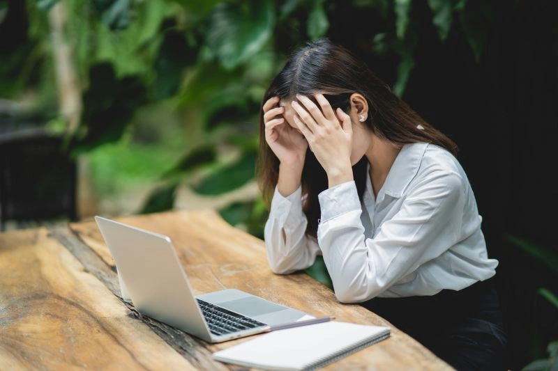 A woman sitting at a desk, holding her head in her hands, appearing overwhelmed by stress. This image may reflect the challenges faced by individuals with both ADHD and depression, as managing attention and mood can be difficult.