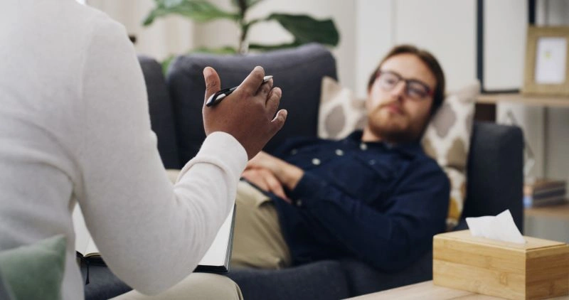 A therapist speaking to a client lying on the couch, possibly addressing emotional concerns related to ADHD and depression. Therapy is a common treatment for managing these conditions together, focusing on cognitive behavioral strategies.