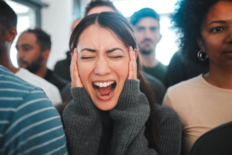 A woman in a crowd, holding her head in distress and appearing overwhelmed. This image symbolizes the emotional and mental struggles faced by individuals with schizoaffective disorder, which involves both mood swings and psychotic symptoms.