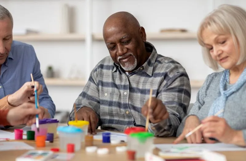 Older adults engaging in a group art session, painting and drawing together. This scene reflects how expressive arts therapy fosters emotional connection and creativity, offering therapeutic benefits in group settings.
