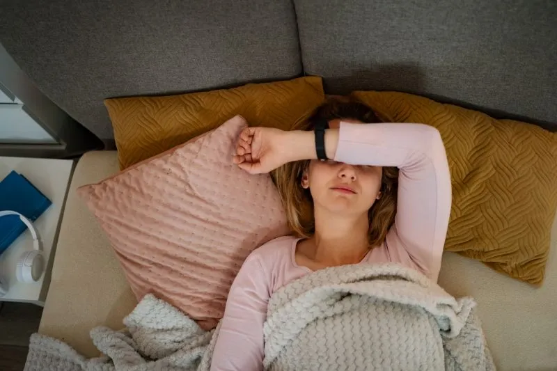 A woman resting in bed with a blanket over her, showing the recovery process that can be supported by residential mental health treatment for adults.