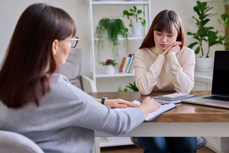 A teenager with a thoughtful expression sitting with a counselor during a session, illustrating the process of cognitive behavioral therapy for teenagers.