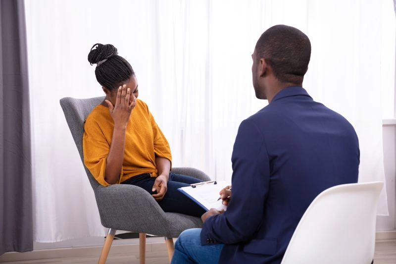 A woman holding her head in frustration while speaking with a counselor, symbolizing the emotional toll that untreated ADHD can take, contributing to anxiety and depression.