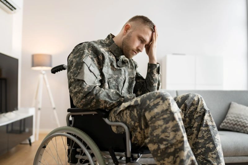 A soldier in a wheelchair holding their head in distress, representing the physical and emotional toll of PTSD and its qualification as a disability for veterans.