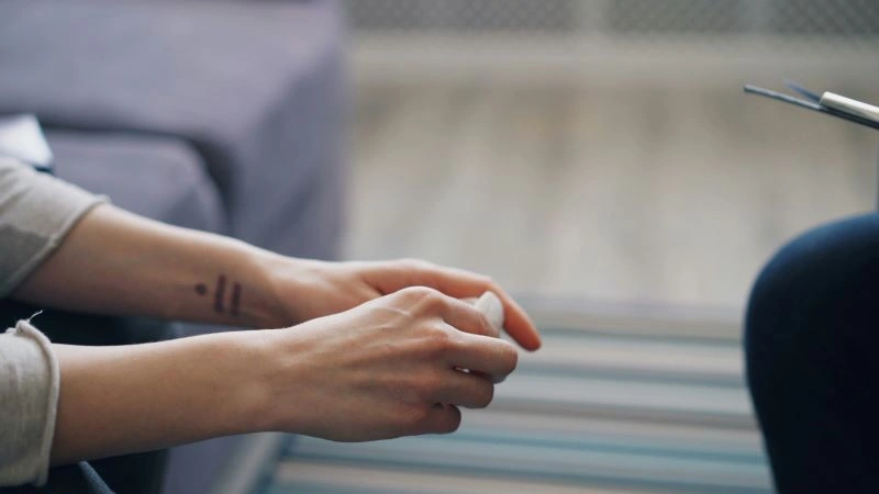 A person sitting with their hands clasped, symbolizing a moment of reflection during cognitive therapy where thoughts and emotions are examined to improve mental health.