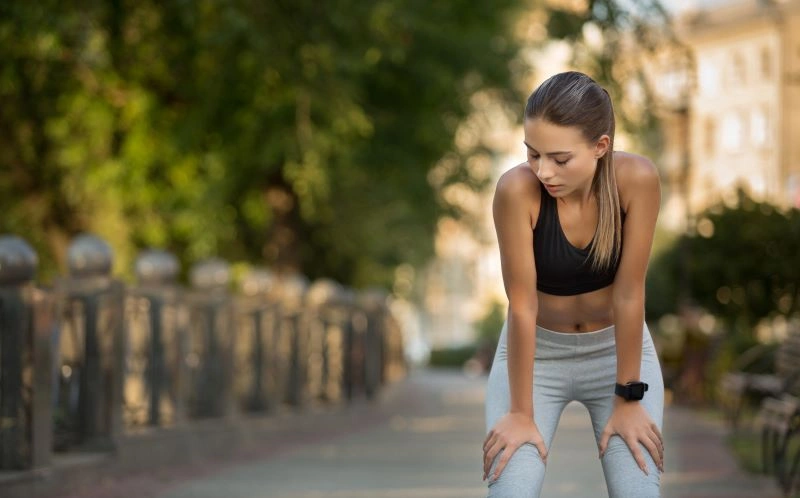 A woman bent over and catching her breath after running outdoors, highlighting the mental health benefits of running as it helps release built-up tension and improves focus.