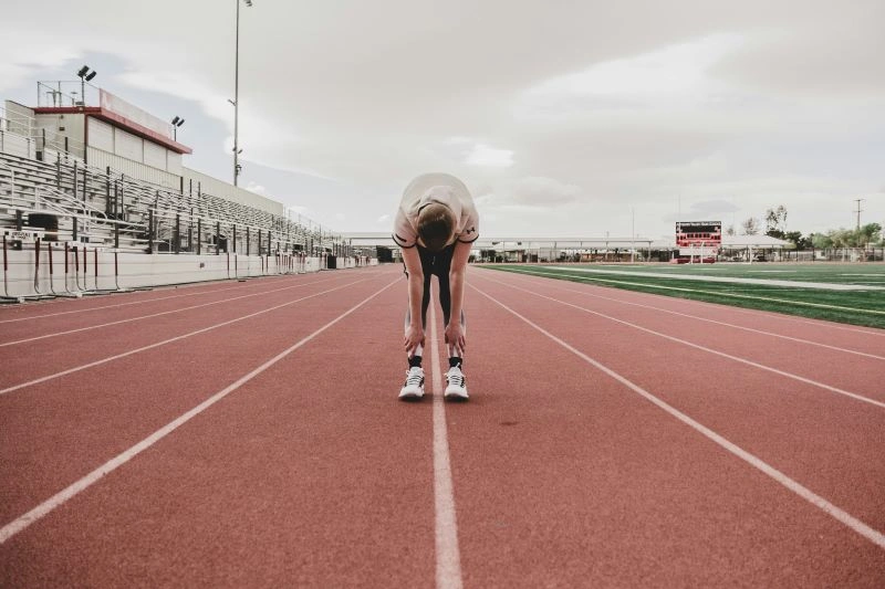 A person stretching after a run on an empty track, illustrating how running can help clear the mind and reduce stress, improving mental health.