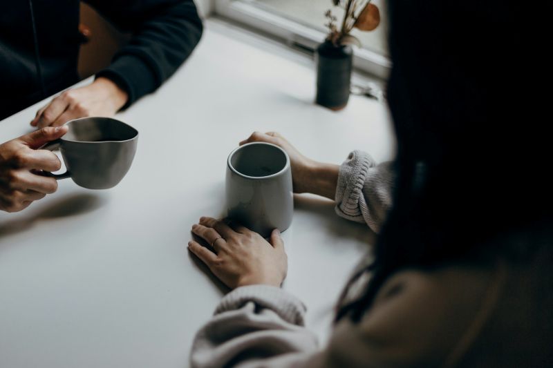 Couples therapy for communication issues shown through an intimate close-up of two people holding mugs while having a calm, reflective conversation