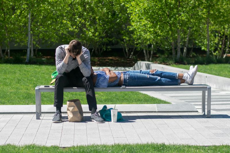 Two people resting on a park bench while one appears distressed, representing symptoms of anhedonia vs depression.