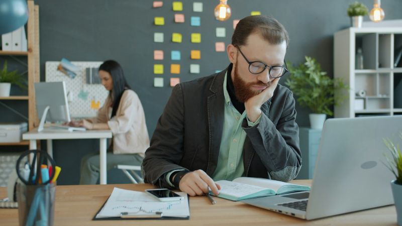 Tired office worker looking disengaged at his desk, highlighting differences between anhedonia vs depression.