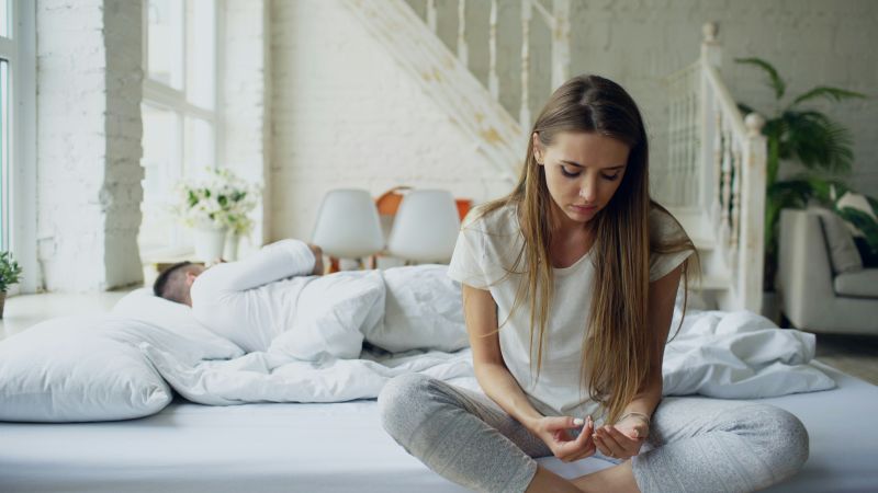 Woman sitting on a bed looking down at her hands, struggling to initiate simple actions, illustrating executive dysfunction and adhd.