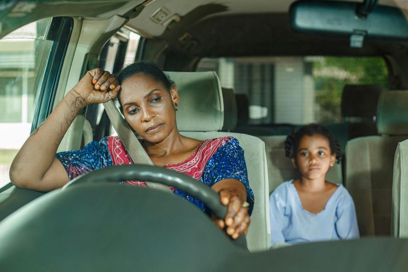 Tired mother sitting in the driver’s seat with a child in the back, reflecting decision fatigue and overwhelm in executive dysfunction and adhd.