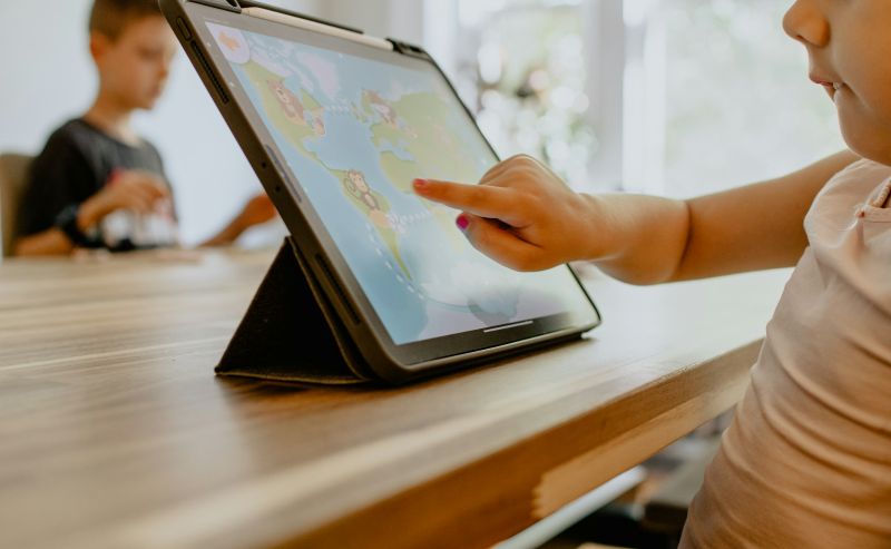 Child interacting with a tablet while distracted in the background, representing difficulties with focus and task initiation in executive dysfunction and adhd.
