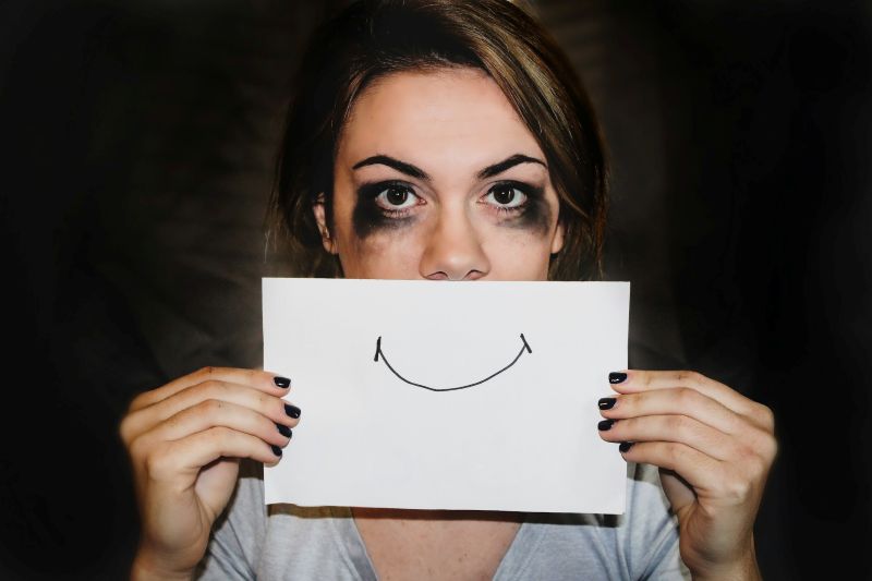 Woman hiding sadness behind a drawn smile, representing the emotional differences in anhedonia vs depression.