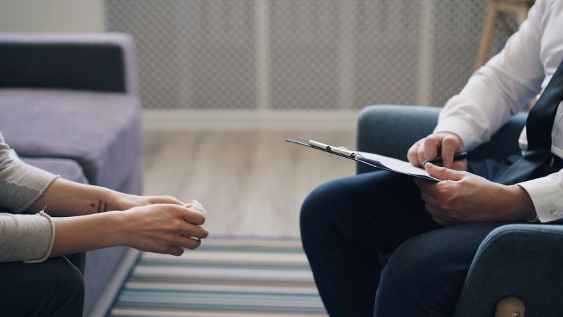psychiatrist meeting with a patient in a clinical office, holding a clipboard during a focused mental health consultation.