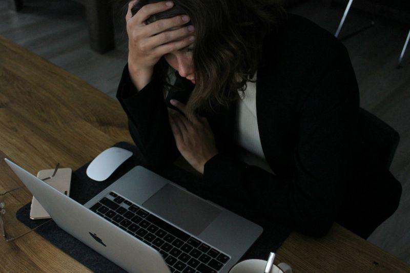 Man overwhelmed at a desk with a laptop, head in hand, showing classic signs of ADHD task paralysis when starting or managing work tasks.