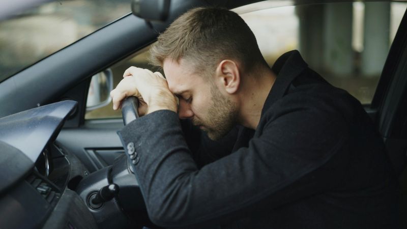 Man in a parked car resting his head on the steering wheel, representing inability to transition into action due to ADHD task paralysis.