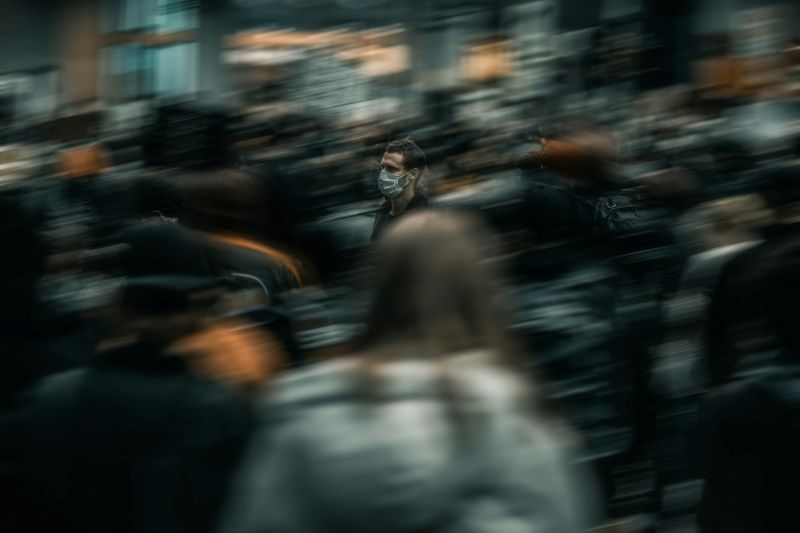 blurred crowd scene with one person wearing a mask, emphasizing feelings of isolation and overwhelm in social environments