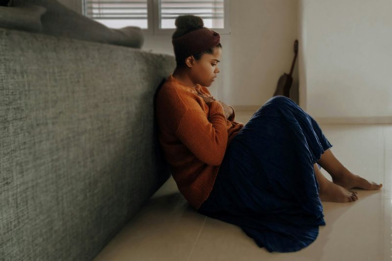 young woman sitting alone on the floor with arms crossed over her chest, showing shyness, withdrawal, and social avoidance behaviors