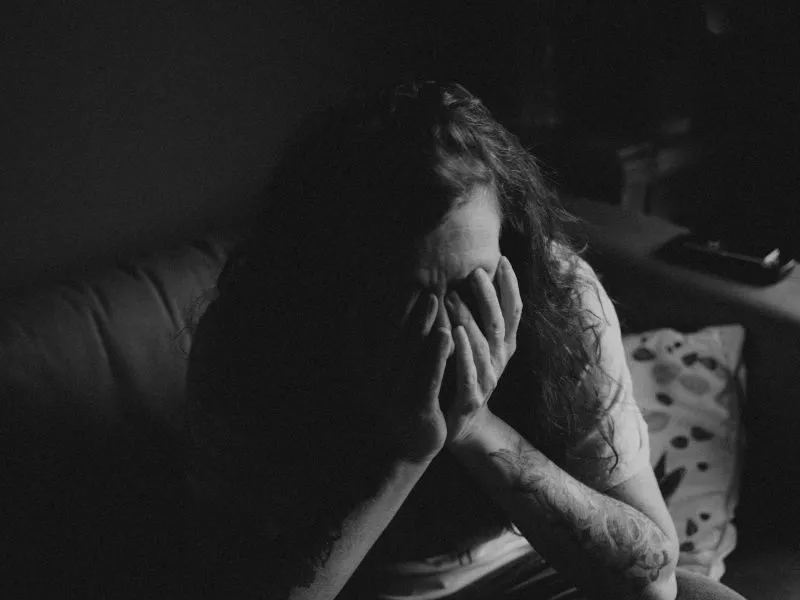 Woman covering her face in a dark room, reflecting major depression vs persistent depressive disorder.