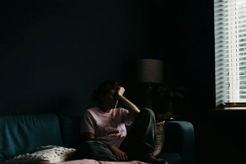 Person experiencing existential anxiety while sitting alone in a dark room with a thoughtful expression