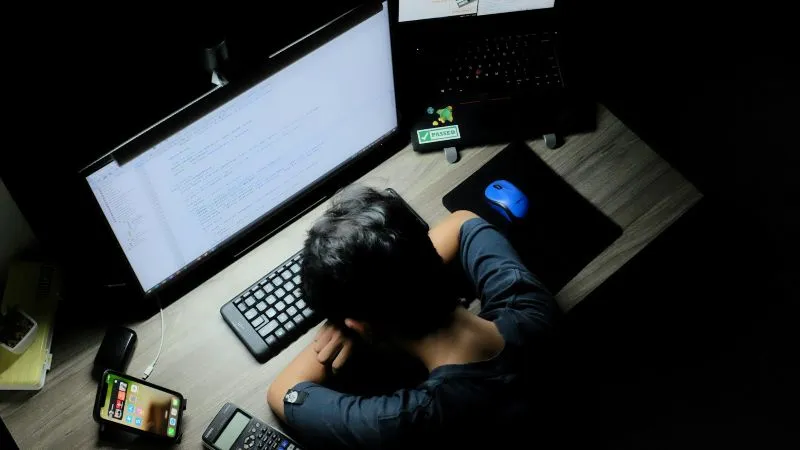 Hypomania vs mania represented by a person resting at a computer desk after working late at night.