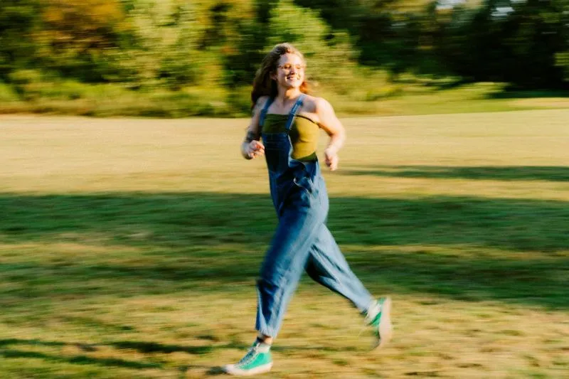 Hypomania vs mania represented by an energetic woman running outdoors across a grassy field.
