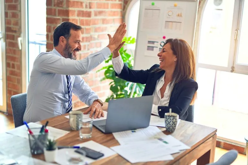 Self awareness and emotional intelligence illustrated by coworkers celebrating successful teamwork with a high five.