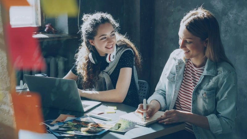 Self awareness and emotional intelligence shown through two women communicating and collaborating at a desk.