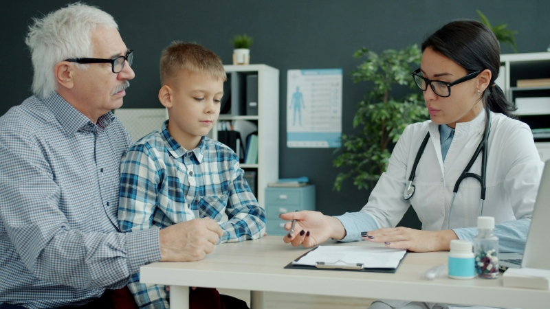 Female doctor discussing how long does ADHD diagnosis take with a young boy and his grandfather during a medical consultation.