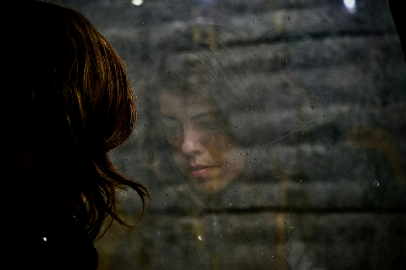 Woman looking at her reflection in a dark mirror, conveying introspection and existential depression.