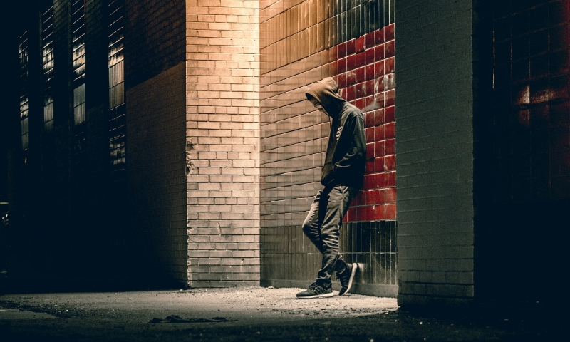 Lonely man standing against a wall in a dimly lit alley, reflecting isolation and existential depression.