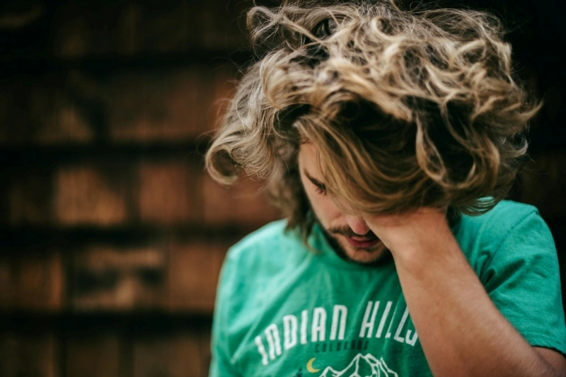Young man holding his forehead in distress, illustrating emotional overwhelm and symptoms discussed in OCD vs ADHD comparisons.