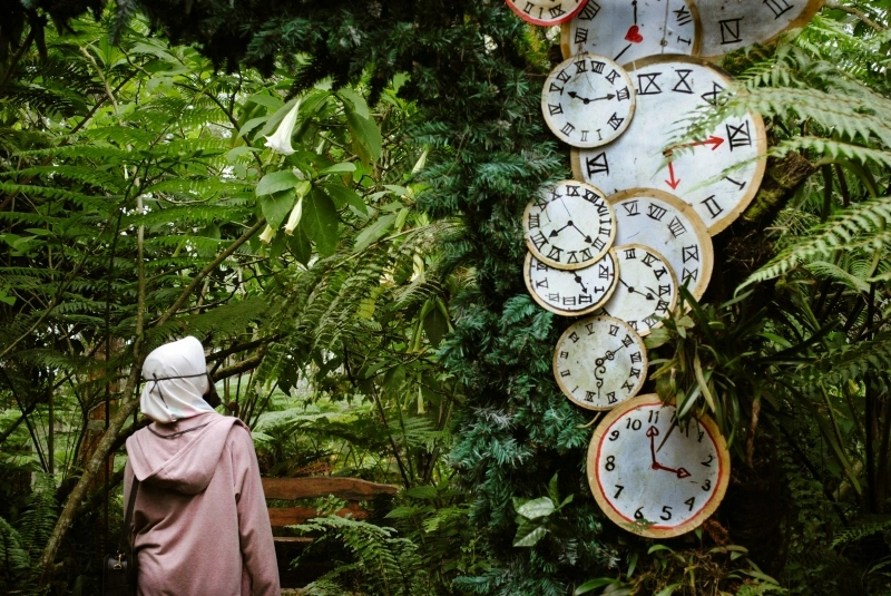 Person standing near a collection of clocks in a garden, symbolizing ADHD and time blindness and difficulties perceiving time.